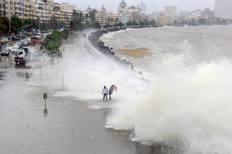 Mumbai: People walk along the shore as a high tide hits the sea wall at Marine Drive, in Mumbai on Saturday.
